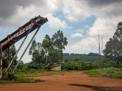 Rusted outdoor belt conveyor material structure positioned on red dirt with forest and cloudy sky in background