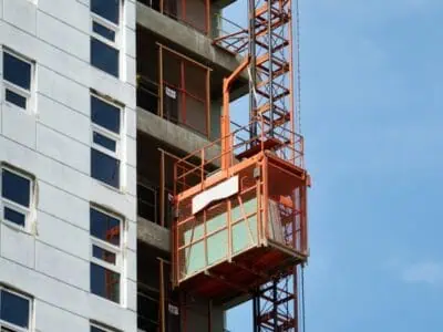 Material hoist construction equipment lifting building supplies along high-rise scaffolding on a commercial site