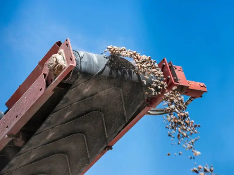 Heavy-duty conveyor belt types transporting and discharging rocks under blue sky.