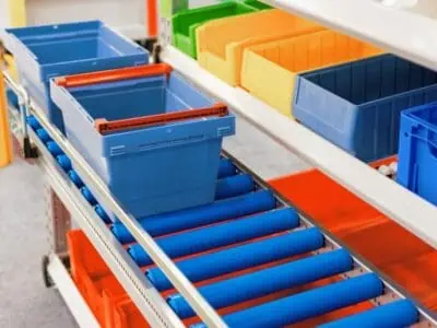 Blue mobile roller conveyor with stackable plastic storage bins in assorted colours on warehouse shelving system.