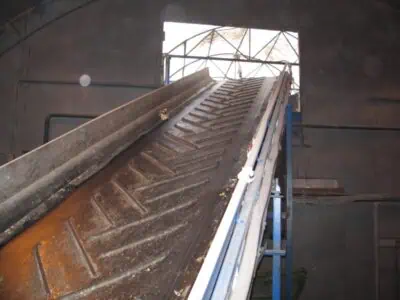 Inclined rubber belt used for waste conveyor hire inside an industrial building during demolition or construction clean-up.