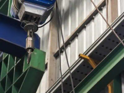 Industrial power lift hoist suspended from steel beam inside a warehouse with visible cable and lifting hook