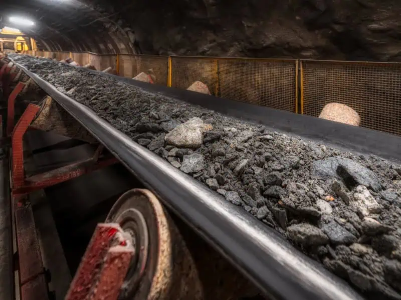 mining conveyor system transporting rocks and minerals through underground tunnel.