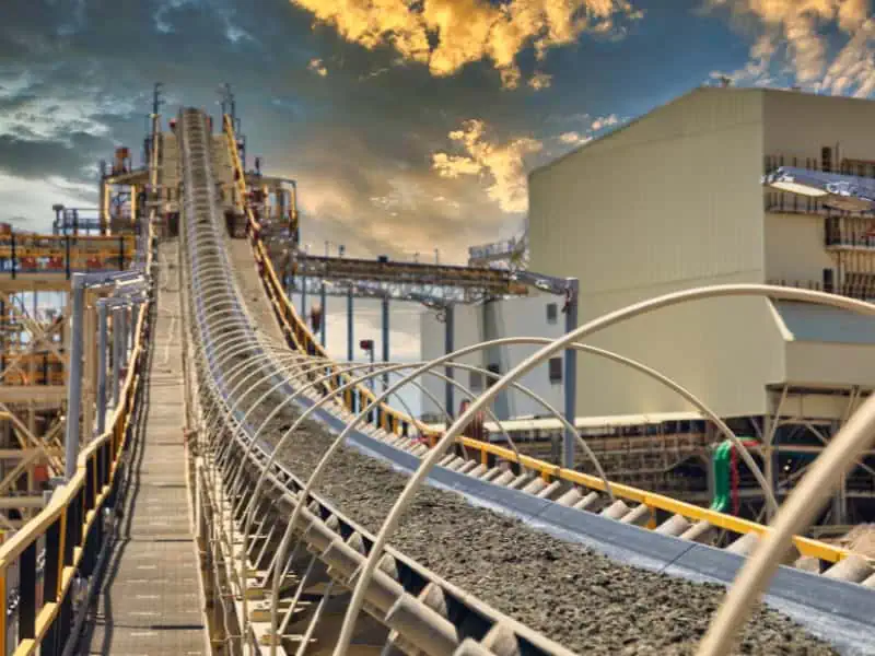 mining conveyor system transporting raw minerals at processing plant under sky.