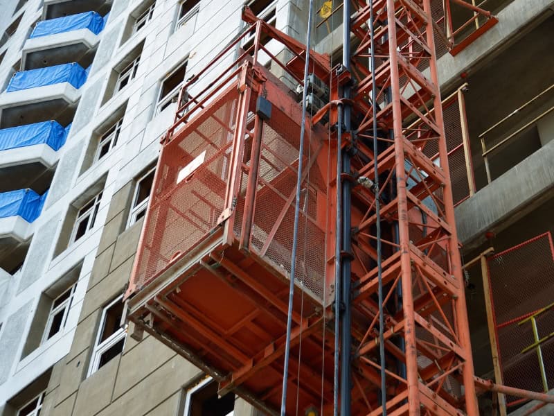red material hoist in construction beside high-rise building