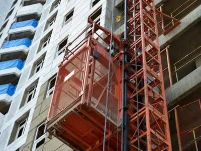 Red builder hoist attached to a high-rise apartment under construction with scaffold and open building levels visible.