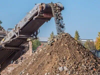 Soil conveyor belt stacking crushed soil and rubble into a large mound on a worksite