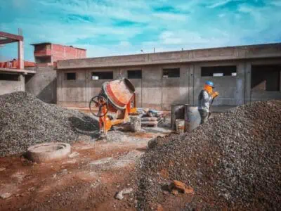 Worker beside aggregate piles and cement mixer on a job site using rock conveyor belt for material movement