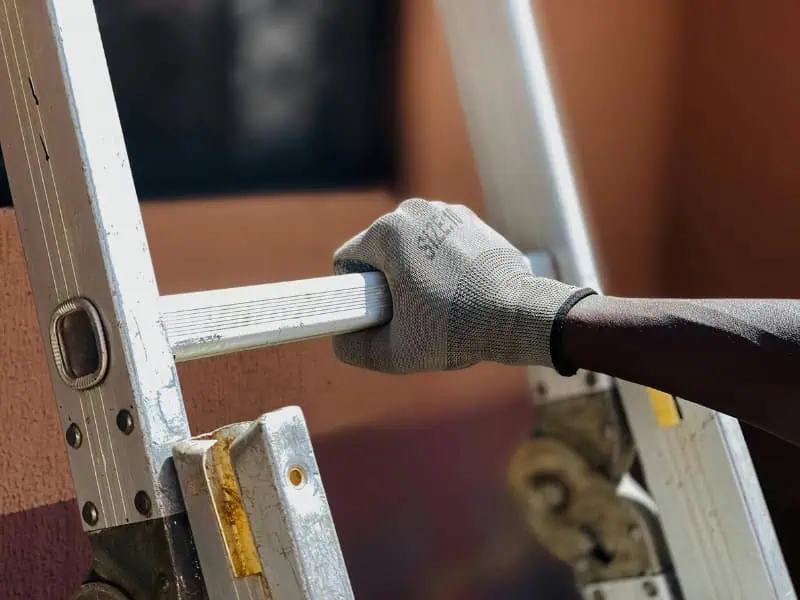 Worker holding Geda Ladder Hoist with safety gloves during setup.