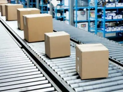 Cardboard boxes moving on a metal mobile roller conveyor inside a warehouse with storage racks.
