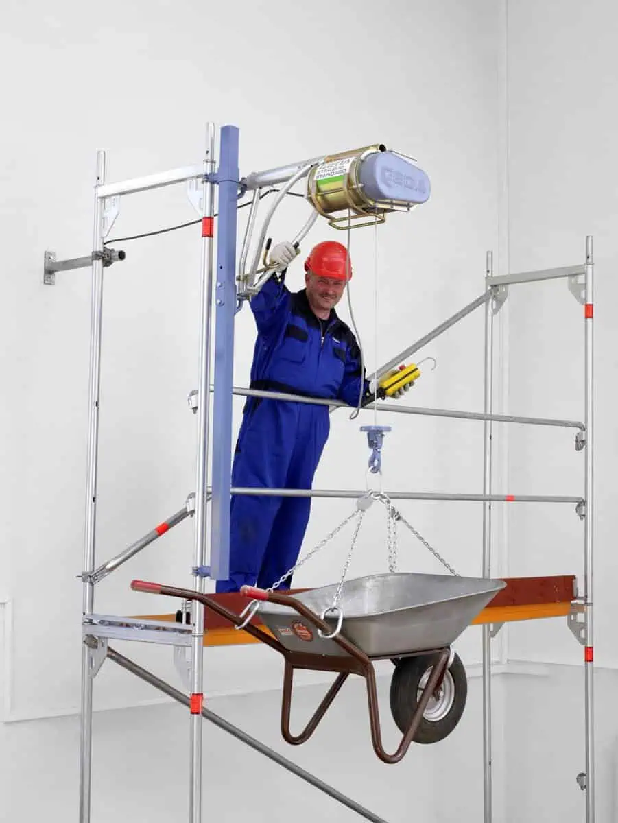 GEDA star hoist mounted on a scaffold frame with a worker lifting a wheelbarrow